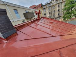 Czerwony dach z blachy, z widokiem na kominy i otaczające budynki.