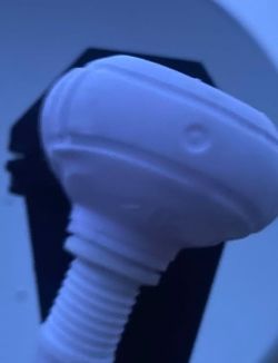 Biały plastikowy zawór wewnątrz ciemnego wnętrza urządzenia.