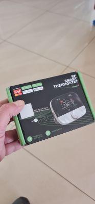 Opakowanie inteligentnego termostatu RF trzymane w dłoni.