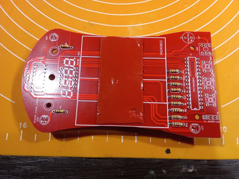 Czerwony obwód drukowany z komponentami elektronicznymi, leżący na pomarańczowej macie.