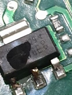 Nahaufnahme eines beschädigten elektronischen Bauteils auf einer Leiterplatte mit teilweise von einem schwarzen Fleck verdeckten Markierungen.