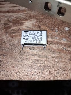 Kondensator X2 0,22 µF 250V~ marki Teapo leżący na płycie wiórowej