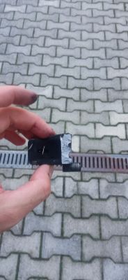 Osoba trzyma w ręku uszkodzony metalowy element, prawdopodobnie część samochodowa.