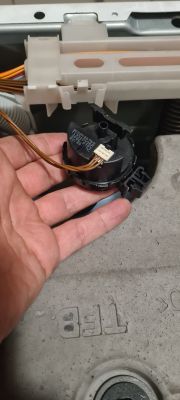Osoba trzyma hydrostat pralki, który jest połączony przewodami elektrycznymi.