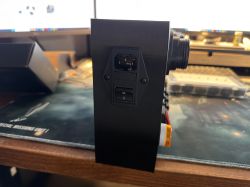 Black device enclosure with an IEC power inlet and rocker switch on the side, on a desk.