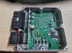 Zbliżenie na sterownik elektroniczny w metalowej obudowie z widocznymi elementami elektronicznymi i złączami.