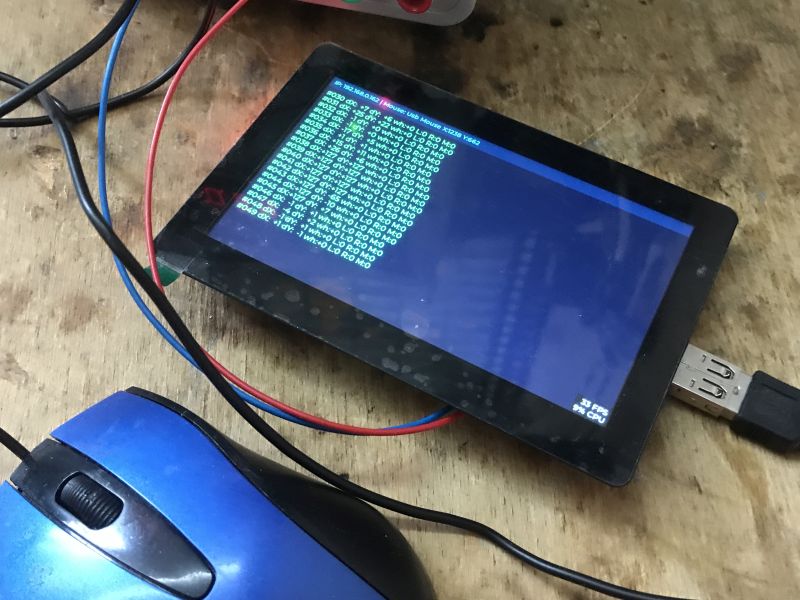 Touchscreen showing green log text on blue background, wired up; blue USB mouse beside it
