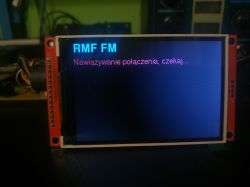Close-up of a touchscreen showing “Connecting, please wait…” for RMF FM
