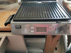 Stalowy grill elektryczny z otwartą pokrywą, widoczne panele sterowania na froncie.