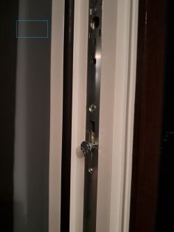 Zbliżenie na metalową listwę zasuwnicy w ramie okiennej z widocznym bolcem.