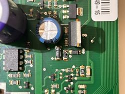 Zbliżenie płytki PCB z kondensatorami, układem scalonym i elementami SMD oraz etykietą z kodem kreskowym.