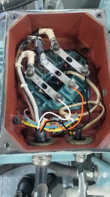Skrzynka przyłączeniowa silnika elektrycznego z widocznymi przewodami i śladami uszkodzenia.