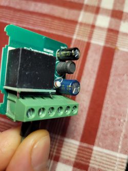 Close-up of a PCB with a green screw terminal block, black relay, and capacitors, held in a hand