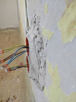 Odsłonięte kable elektryczne i gniazdko w ścianie z nierównym tynkiem.