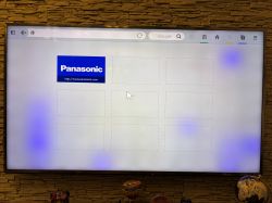 Telewizor Panasonic na ścianie, jasny ekran z fioletowymi plamami i stroną startową przeglądarki.