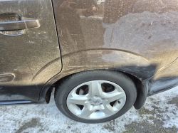 Rear wheel and fender of a black car, with visible scuffs and dirt on the body panel.