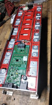 Otwarty moduł akumulatora w czerwonej obudowie z płytką elektroniki i szeregiem ogniw po bokach