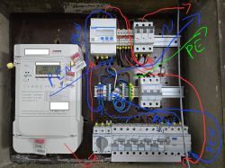 Widok skrzynki elektrycznej z licznikiem i elementami instalacji z opisanymi połączeniami.