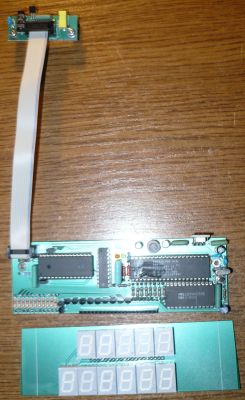 Płytka PCB z układami scalonymi i taśmą, pod nią dwa białe wyświetlacze 7‑segmentowe