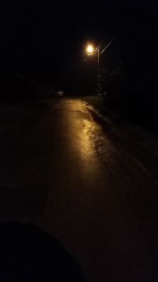 Oświetlona latarnią ulica nocą po deszczu, z mokrą nawierzchnią odbijającą światło