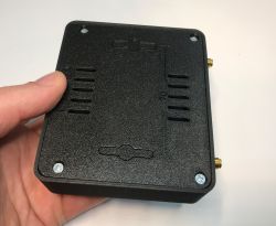 Czarna plastikowa obudowa elektroniczna z widocznymi śrubami montażowymi i otworami wentylacyjnymi, trzymana w dłoni.