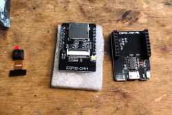 ESP32-Cam with Camera and Adapter on Wooden Table ESP32-Cam with OV2640 camera and ESP32-Cam-MB adapter on a wooden table